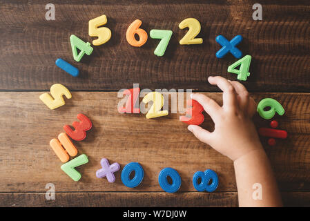child hand holding a colorful plastic toy numbers on a wooden table. children learning counting numbers 123. concept of early education Stock Photo