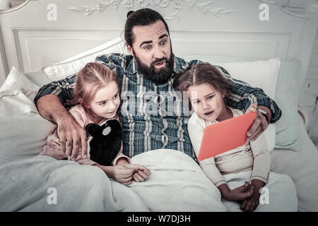 Interested in movie dad watching film on a tablet with daughters in bed Stock Photo