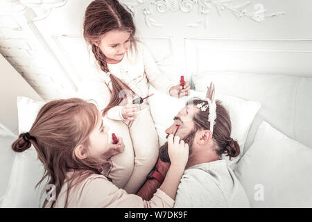 Happy smiling girls painting on dads face while he naps Stock Photo