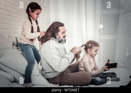 Family of father and two daughters braiding each others hair Stock Photo