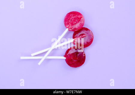 Three Red Lollipops on a Violet Color Background. Top View Flat Lay Background. Stock Photo