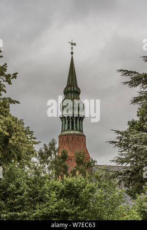 a copper spire on an onion dome among the green trees against a greyish sky at Frederiksvarek, Denmark, July 30, 2019 Stock Photo