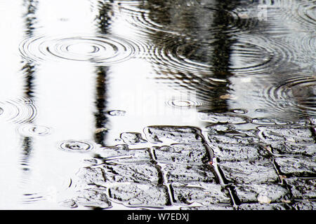 Detail of  rain drops in a puddle and reflections on a cobbled road Stock Photo