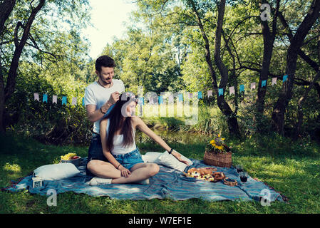 Young couple on a picnic sitting on a blanket in the park The man put on her head flower crown Selective focus Stock Photo