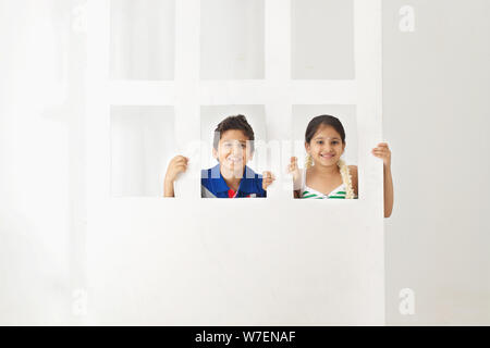 Children peeking behind a door Stock Photo