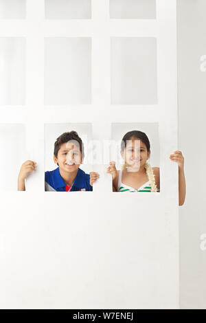 Children peeking behind a door Stock Photo