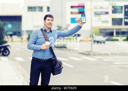 Young man using mobile phone app waiting for rideshare – Millennial business man with hand up calling taxi hailing from sidewalk Stock Photo