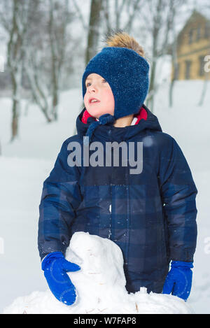 portrait of little boy in winter. the child is dressed in winter clothes hat, jacket and mittens. kid makes a snowman and plays Stock Photo