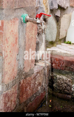 Faucet in a brick wall and running water Stock Photo