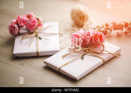 Handmade present box wrapped in paper with branch of roses. Eucalyptus branch and rustic hemp cord spools on background Stock Photo