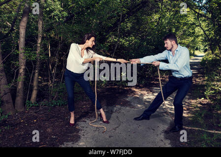 Business woman and business man pulling rope in the city park in formal wear Selective focus Stock Photo