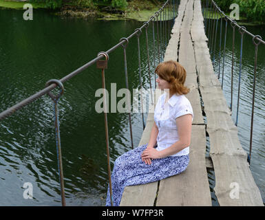 Woman sitting on a wooden bridge over the river Stock Photo