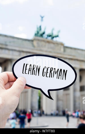 closeup of the hand of a young man showing a speech bubble with the text learn German written in it, in front of the Brandenburg Gate in Berlin, Germa Stock Photo