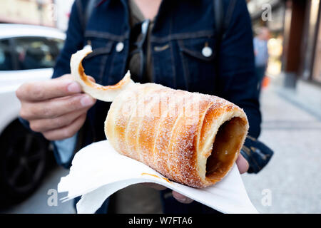 closeup of a yougn caucasian man eating a trdelnik, a typical spit cake, in the old town of Prague, Czech Republic Stock Photo