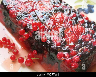 A glazed terrine of summer berries and fruits served as a light dessert on a pretty plate and garnished with redcurrants. Stock Photo