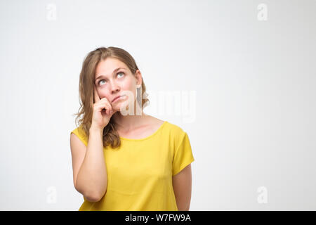 Pretty thoughtful caucasian young woman looks with doubt wears yellow t shirt, trying to make right decision. Pensive youngster being deep in thoughts Stock Photo