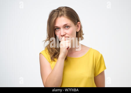 Pretty thoughtful caucasian young woman looks with doubt wears yellow t shirt, trying to make right decision. Pensive youngster being deep in thoughts Stock Photo