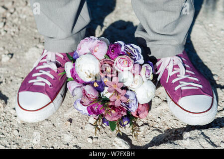 Wedding details in the form of purple sneakers and a purple wedding bouquet. Stock Photo