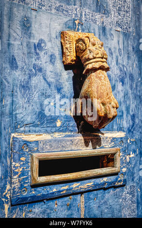 Door knocker in the form of a hand coming out of a decorative ruffled cuff of a sleeve. A letter box opening is beneath the knocker. Stock Photo