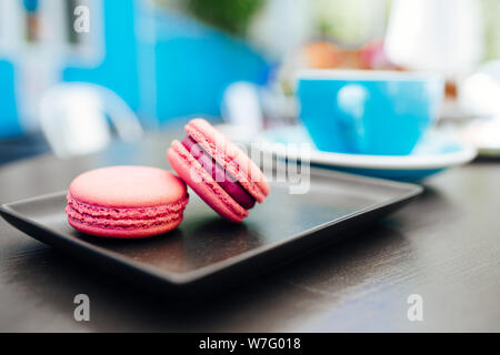 Sweet, fresh macarons with coffee in a blue cup on a black table Stock Photo