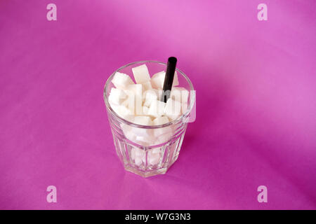 Glass full of sugar cubes  on purple background. Diabetes, sugar disease, unhealthy food, diet concept. Copy space Stock Photo