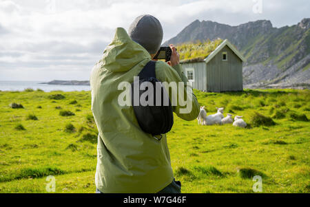Man photographer taking picture typical norwegian house with grass on the roof. Beautiful colored village house. Travel and hobbies concept. Stock Photo