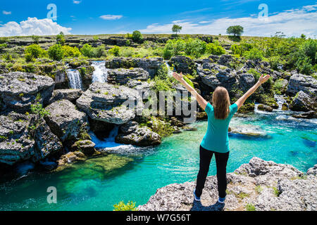 Montenegro, Pretty blonde young woman standing with arms stretched amazed at azure water of cijevna river riverside in spectacular nature landscape on Stock Photo