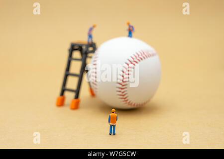 Miniature people Construction worker with baseball on Abstract background and red stitching baseball. White baseball with red thread.Baseball is a nat Stock Photo