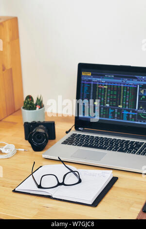 Opened laptop with files manager on the screen, planner, glasses and digital camera on table of photographer Stock Photo