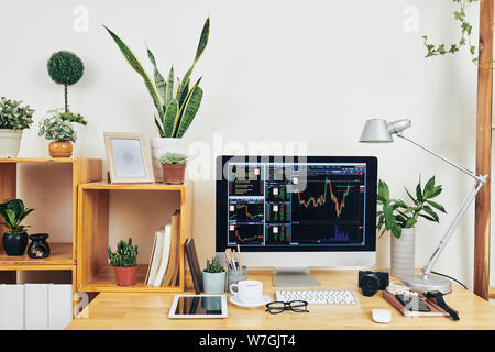 Computer with chart with stock market data on screen, gadgets, textbooks and houseplants in home office of business person Stock Photo