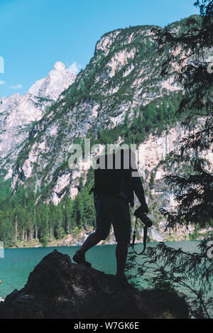 man climbing by rocks to shoot beautiful landscape of lake and mountains. photographer activities Stock Photo