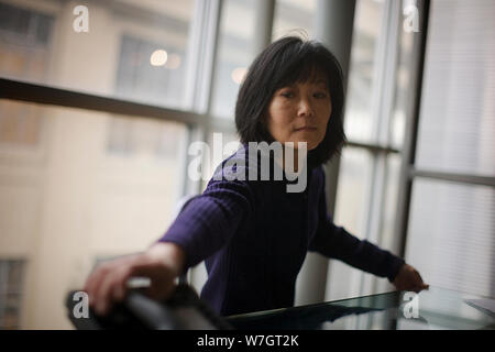 Mid-adult woman reaching towards a telephone sitting on the table inside a boardroom. Stock Photo