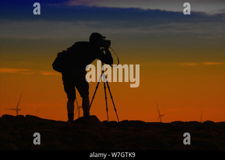 A photographer in silhouette using a DSLR camera and tripod taking a ...