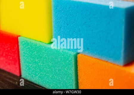Sponges of different colors in dark background forming a wall. Pieces of dishcloth laid as bricks on dark background Stock Photo