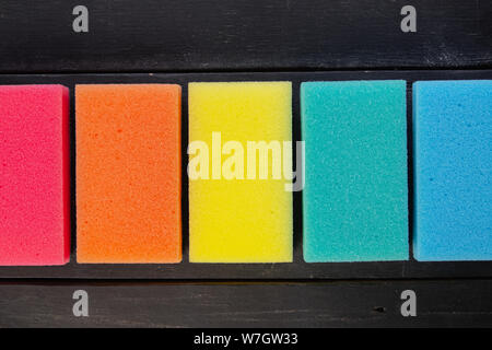 Sponges of different colors in dark background, top view. Five pieces of dishcloth laid in row on dark background, shot from above Stock Photo
