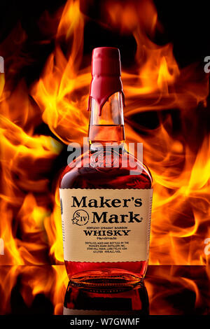 A bottle of Maker's Mark whiskey stands on a glass bar top against the background of a fire flame. Stock Photo