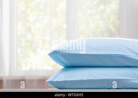 Closeup of two blue pillows lie on a dresser against the background of a blurred window. Copy space. Stock Photo