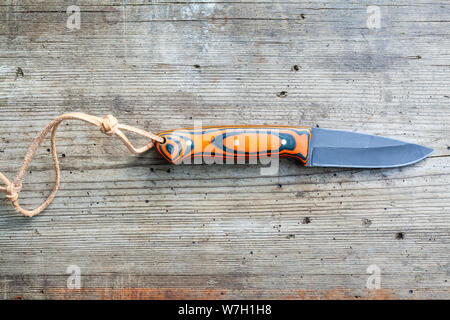 hand forged blackened steel knife with homemade epoxy and orange fabric handle with leather strap on old wooden board Stock Photo