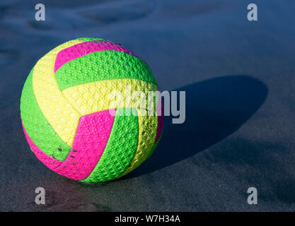 Bright multi-colored ball for beach volleyball on the sea dark sand. It is lit by the sun's rays. Stock Photo