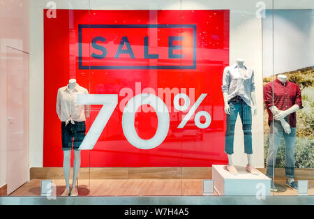 Seasonal discounts in the store. Big red banner with text SALE 70 percent on a shop windows and mannequins dressed in casual clothes. Black friday in Stock Photo