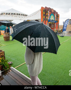 North Berwick, East Lothian, Scotland, UK, 6 August 2019. UK Weather: Torrential downpours during the festival with visitors to the seaside Fringe by the Sea in North Berwick harbour. A woman with a large black umbrella takes shelters near the Spiegeltent in the rain Stock Photo