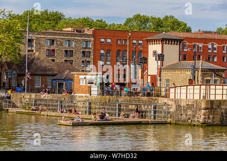 People relaxing in the sun on Bristol's harbourside next to the Victorian Grade 2 Listed Prince Street swing bridge. Bristol, UK. July 2019. Stock Photo