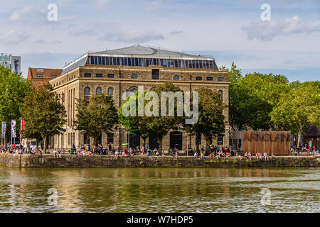 People enjoying the sun outside the Arnolfini, a contemporary arts centre and gallery on the harbourside, Bristol, UK. July 2019. Stock Photo