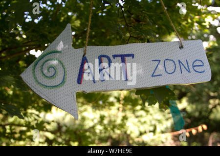 Arrow pointer with an inscription Art zone hanging on a tree on a background of meadow, selective focus Stock Photo