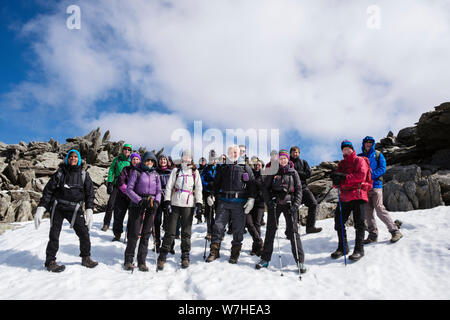 Group of happy hikers hiking together in snow on Glyder Fawr in mountains of Snowdonia National Park. Ogwen, Gwynedd, Wales, UK, Britain Stock Photo