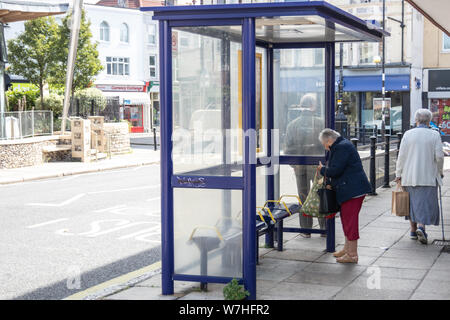 An elderly lady waiting at a bus stop for her bus to arrive Stock Photo