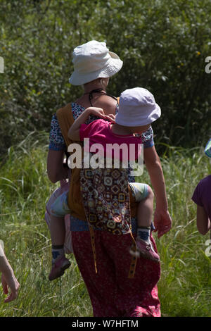 Kharkiv, Ukraine - July 09, 2019: Rear view of a mother in panama carrying a child in panama on her back along a path in nature Stock Photo