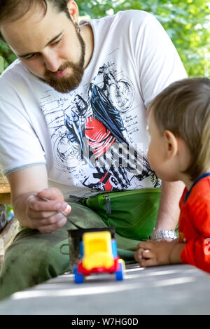 Kharkiv, Ukraine - July 09, 2019: A young man feeds a little boy with a spoon from a mug, dad and son outdoors Stock Photo