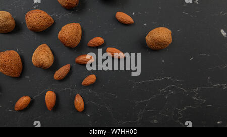 Top down view, almonds scattered over black working board, some of them whole in shell, others opened, space for text, right down corner. Stock Photo