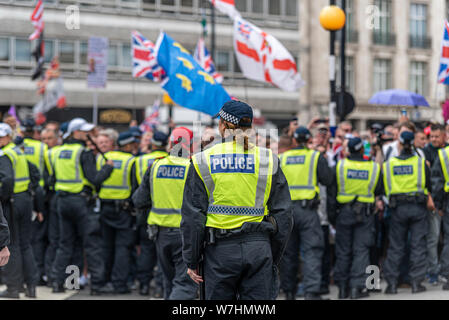 Crowds of angry people at Free Tommy Robinson protest rally In London, UK, behind police cordon. Separate lone female officer behind line of males Stock Photo
